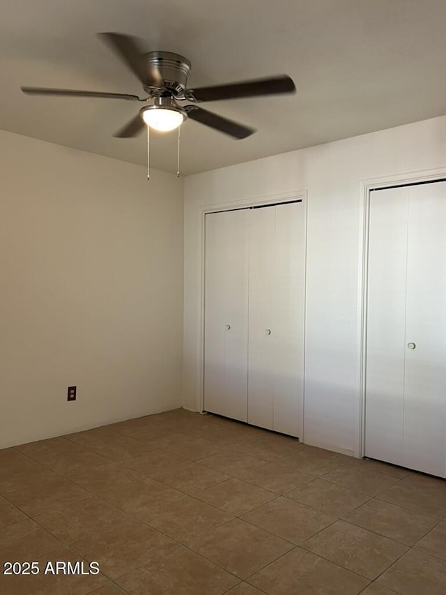 unfurnished bedroom with tile patterned flooring, a ceiling fan, and multiple closets