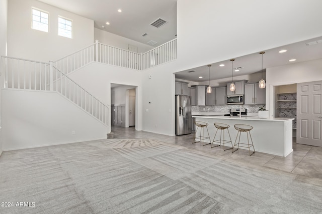 kitchen featuring an island with sink, light colored carpet, gray cabinetry, backsplash, and stainless steel appliances