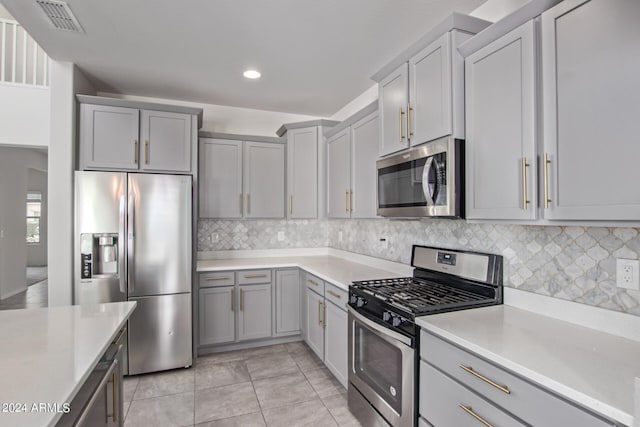 kitchen featuring appliances with stainless steel finishes, gray cabinets, tasteful backsplash, and light tile floors