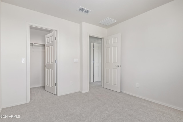 unfurnished bedroom with a walk in closet, light carpet, and a closet