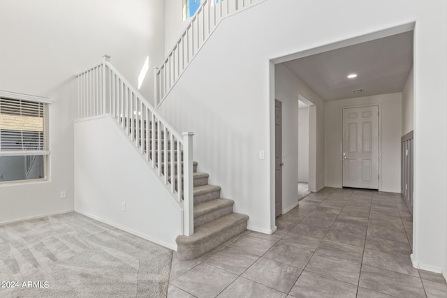 stairway with light carpet and a towering ceiling