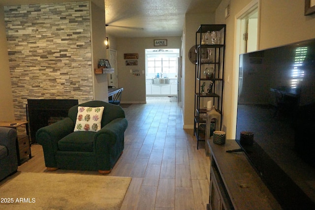 living room with light wood-type flooring, a fireplace, a textured ceiling, and baseboards