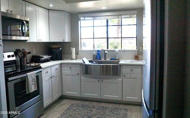 kitchen with appliances with stainless steel finishes, light wood finished floors, light countertops, a sink, and white cabinetry