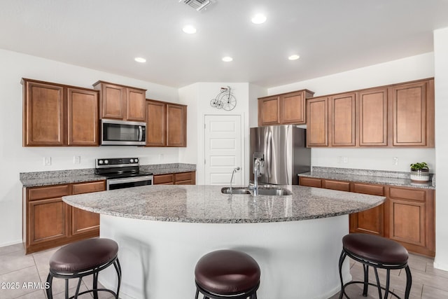 kitchen with an island with sink, a breakfast bar area, appliances with stainless steel finishes, light stone counters, and sink