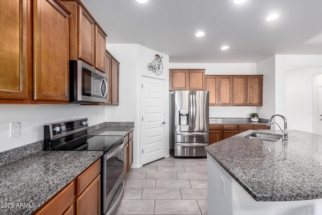 kitchen featuring dark stone countertops, a center island with sink, sink, stainless steel appliances, and light tile patterned floors