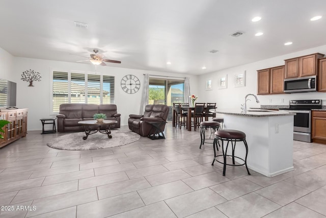 kitchen featuring appliances with stainless steel finishes, stone countertops, a kitchen island with sink, ceiling fan, and a breakfast bar area