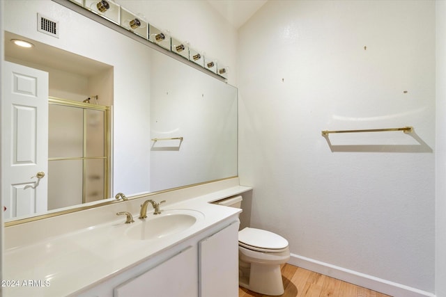 bathroom featuring vanity, hardwood / wood-style flooring, toilet, and a shower with shower door