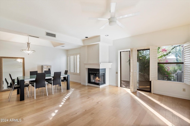 dining area featuring ceiling fan, a healthy amount of sunlight, a multi sided fireplace, and light hardwood / wood-style flooring