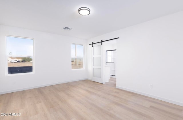 spare room with a barn door and light hardwood / wood-style floors