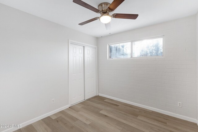 spare room with light hardwood / wood-style floors, ceiling fan, and brick wall