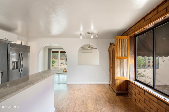 unfurnished dining area featuring ceiling fan, arched walkways, and light wood-style floors