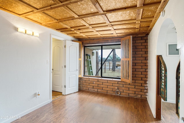 empty room featuring brick wall, arched walkways, baseboards, and wood finished floors