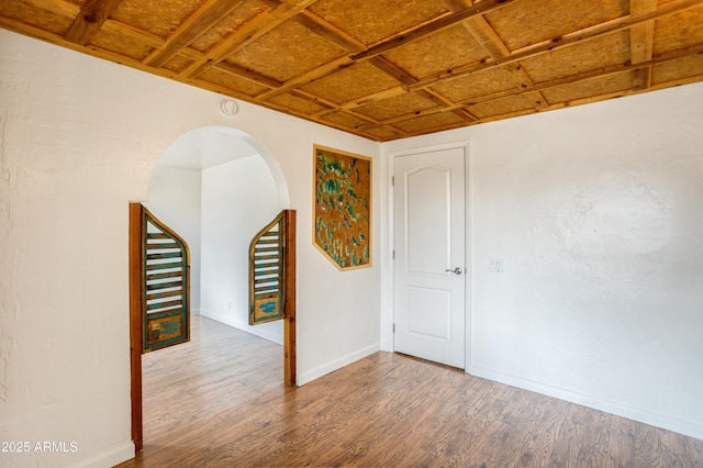 spare room with arched walkways, baseboards, and wood finished floors