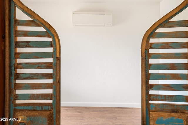 stairs with arched walkways, a wall unit AC, baseboards, and wood finished floors