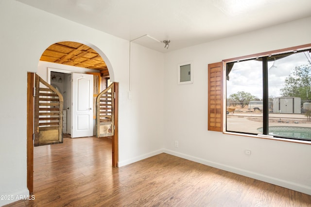 empty room with stairs, arched walkways, baseboards, and wood finished floors