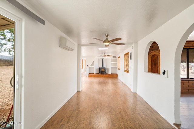 hallway featuring wood finished floors, baseboards, a wall unit AC, and arched walkways