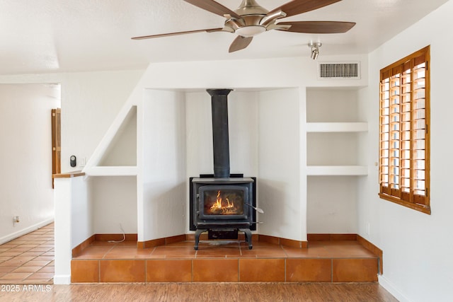 unfurnished living room featuring visible vents, tile patterned flooring, baseboards, ceiling fan, and a wood stove