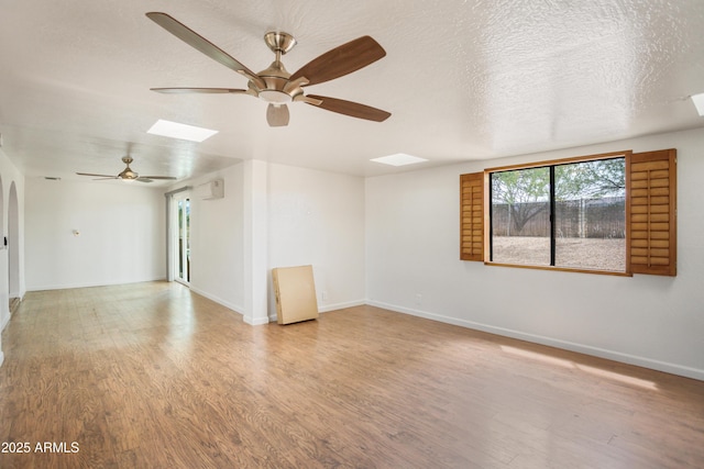 empty room featuring wood finished floors, a ceiling fan, a textured ceiling, baseboards, and a wall mounted AC