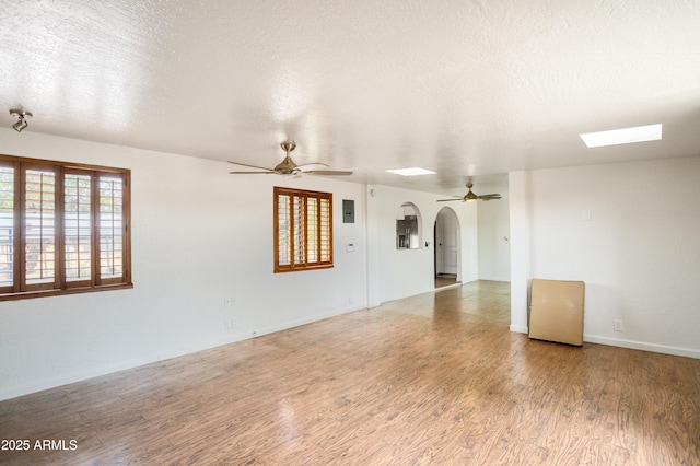 unfurnished room featuring a wealth of natural light, arched walkways, a ceiling fan, and wood finished floors