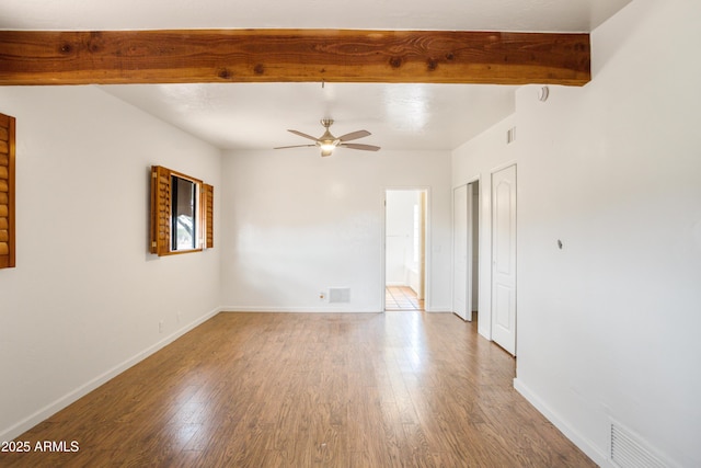unfurnished room with wood finished floors, a ceiling fan, beam ceiling, visible vents, and baseboards