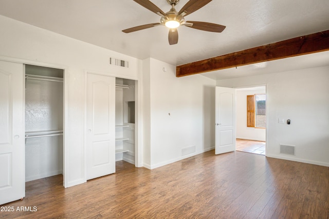 unfurnished bedroom featuring beam ceiling, baseboards, visible vents, and wood finished floors