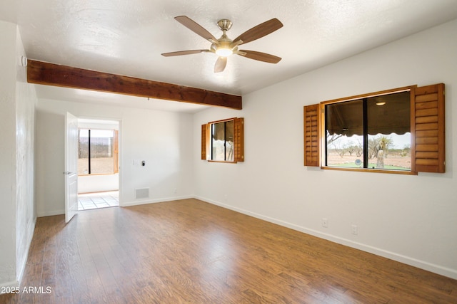 spare room with wood finished floors, a ceiling fan, beam ceiling, visible vents, and baseboards