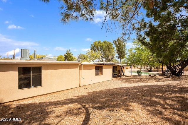 exterior space featuring central AC, stucco siding, and an outdoor pool