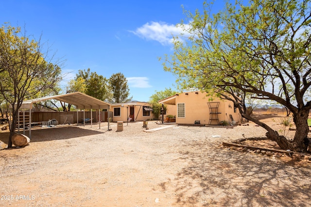 rear view of property with dirt driveway, a detached carport, stucco siding, and fence