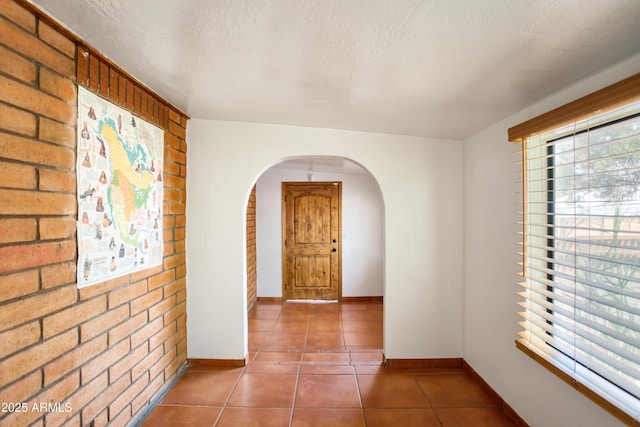 hall featuring brick wall, tile patterned flooring, arched walkways, and a healthy amount of sunlight