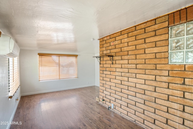 unfurnished living room featuring wood finished floors, baseboards, a wall mounted AC, and brick wall