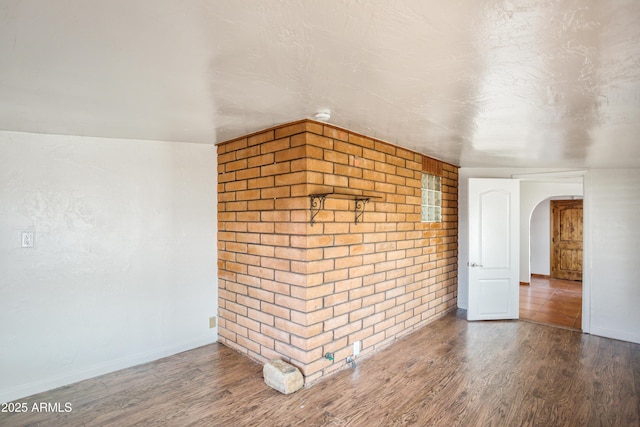 spare room with wood finished floors, baseboards, arched walkways, and brick wall