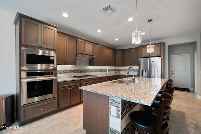 kitchen featuring appliances with stainless steel finishes, sink, an island with sink, light stone counters, and tasteful backsplash