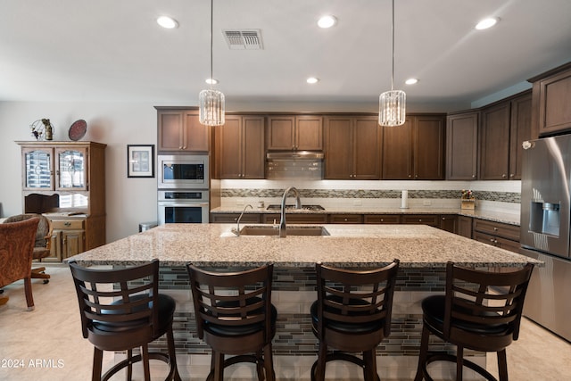 kitchen featuring an island with sink, light stone countertops, stainless steel appliances, and decorative light fixtures