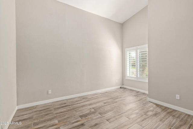 unfurnished room featuring light wood-style flooring, baseboards, and vaulted ceiling