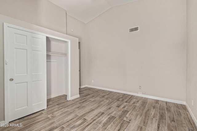 unfurnished bedroom featuring wood finished floors, visible vents, baseboards, vaulted ceiling, and a closet