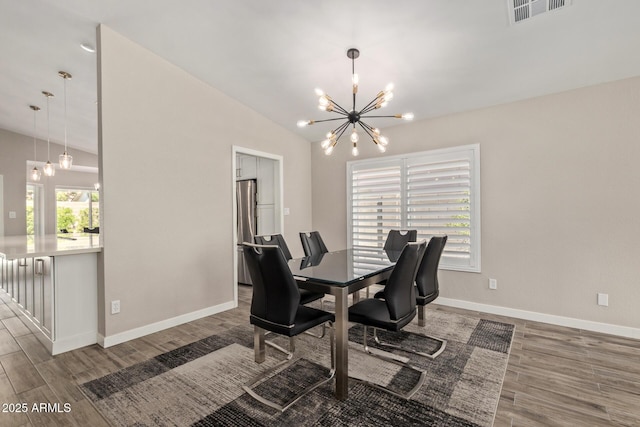 dining space with visible vents, a notable chandelier, wood finished floors, baseboards, and lofted ceiling