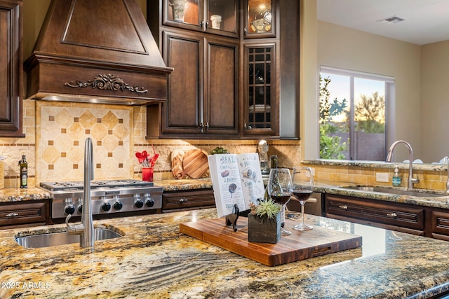 kitchen featuring light stone counters, custom exhaust hood, dark brown cabinets, and a sink