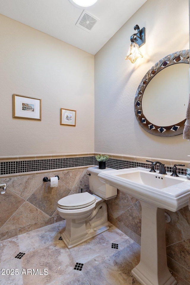 bathroom featuring a sink, visible vents, toilet, and tile walls
