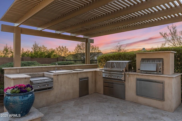 patio terrace at dusk featuring fence, exterior kitchen, area for grilling, and a pergola