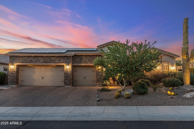 view of front of property featuring roof mounted solar panels, driveway, stone siding, and an attached garage