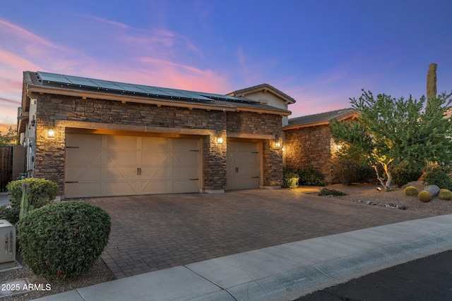 view of front of home with solar panels, driveway, an attached garage, and stone siding