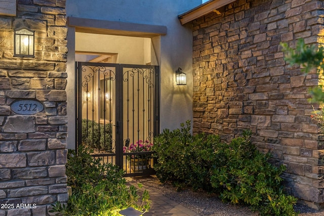 entrance to property with stone siding, stucco siding, and a gate