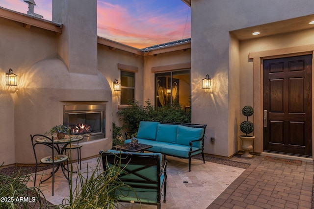 exterior entry at dusk featuring an outdoor living space with a fireplace, stucco siding, and a patio area