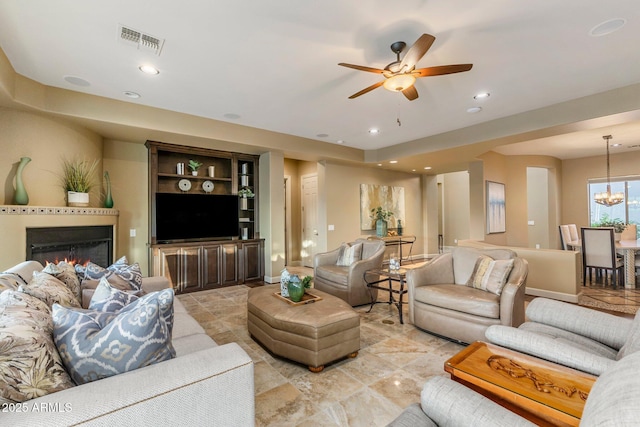 living area with a glass covered fireplace, visible vents, ceiling fan with notable chandelier, and recessed lighting