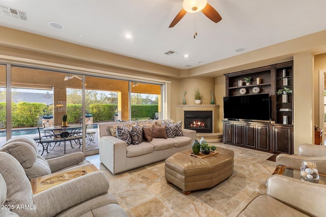 living room with a glass covered fireplace, visible vents, and a ceiling fan