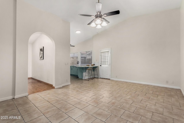 unfurnished living room with arched walkways, high vaulted ceiling, baseboards, and a ceiling fan