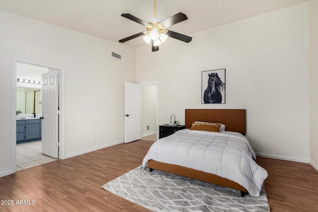 bedroom with visible vents, ensuite bath, light wood finished floors, baseboards, and a towering ceiling