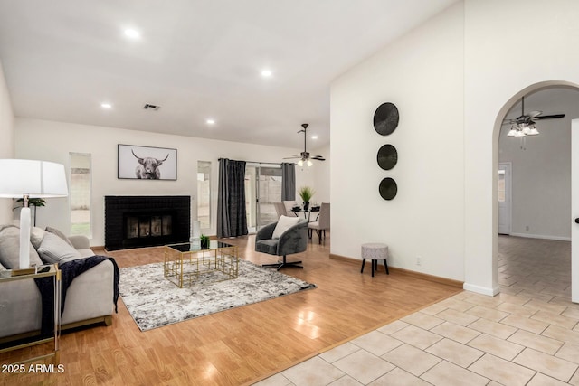 living area featuring wood finished floors, arched walkways, ceiling fan, and a fireplace