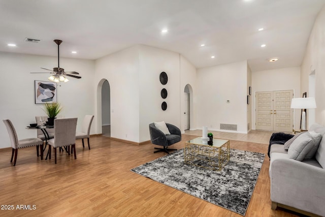 living area featuring visible vents, arched walkways, a ceiling fan, and light wood finished floors