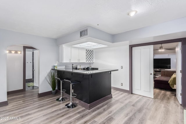 kitchen with a textured ceiling, white cabinets, a kitchen breakfast bar, kitchen peninsula, and light hardwood / wood-style flooring